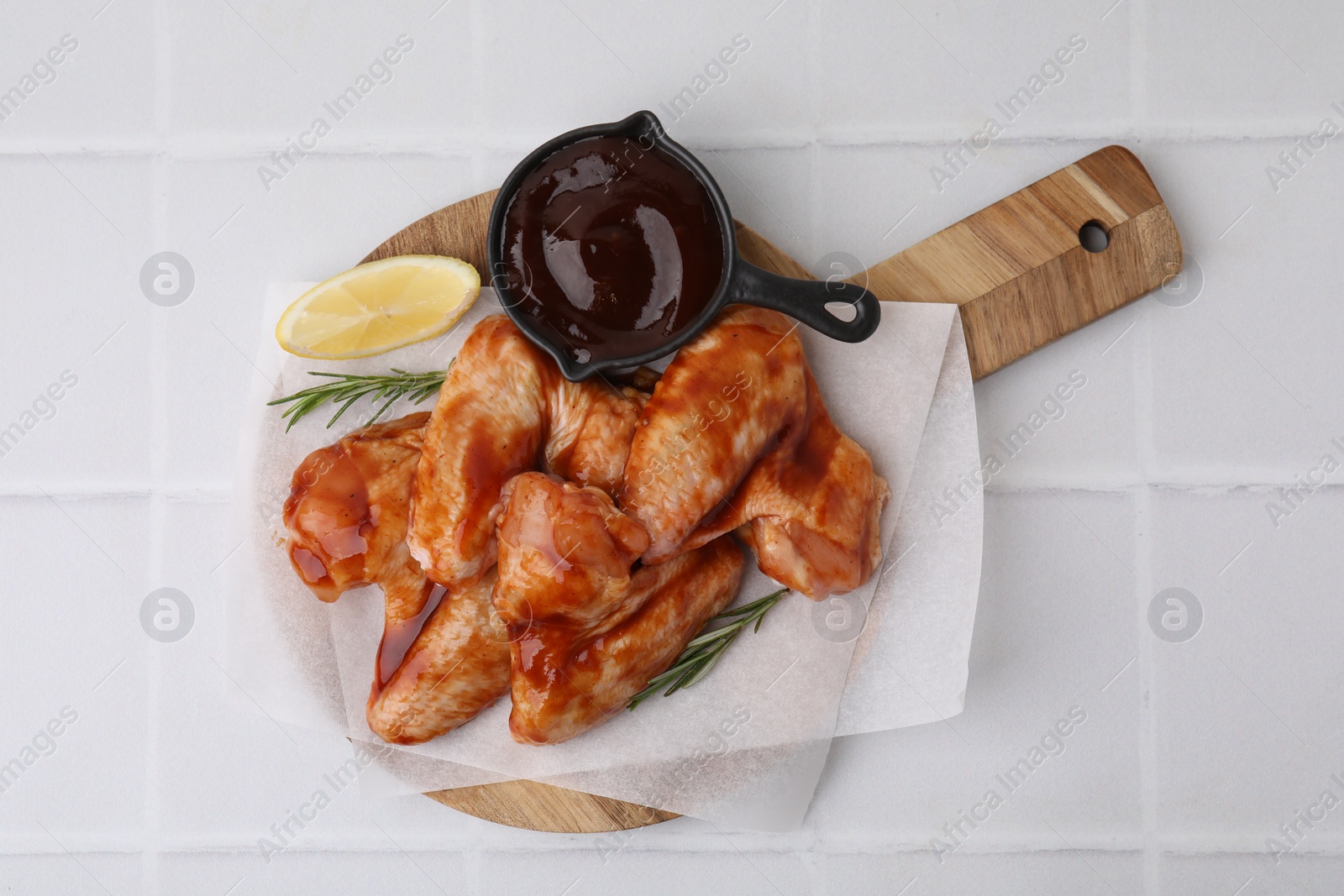 Photo of Raw chicken wings, rosemary, lemon and marinade on light tiled table, top view