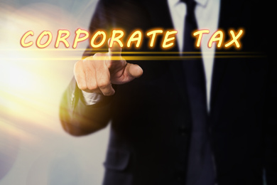 Image of Corporate tax concept. Man touching virtual screen on color background, closeup