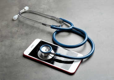 Photo of Modern smartphone with broken display and stethoscope on table. Device repair service