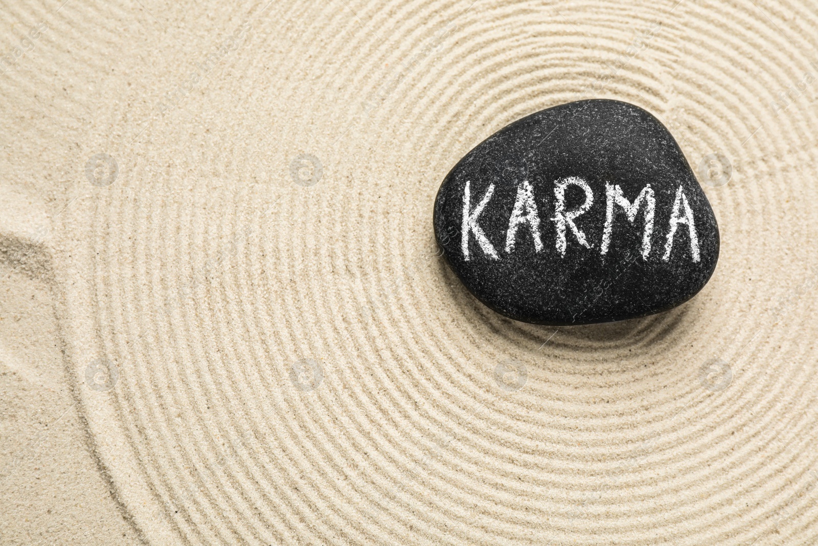 Photo of Stone with word Karma and circles on sand, top view. Space for text