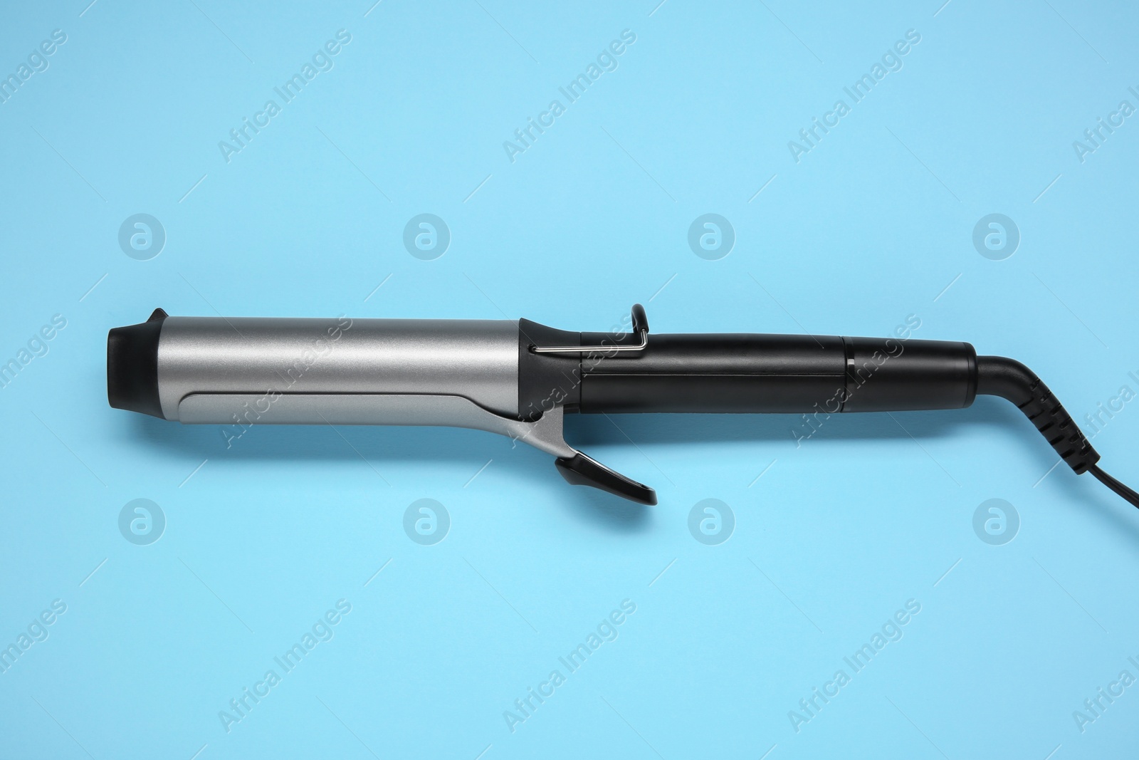 Photo of Hair styling appliance. One curling iron on light blue background, top view