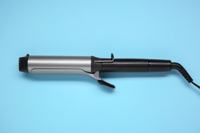 Hair styling appliance. One curling iron on light blue background, top view