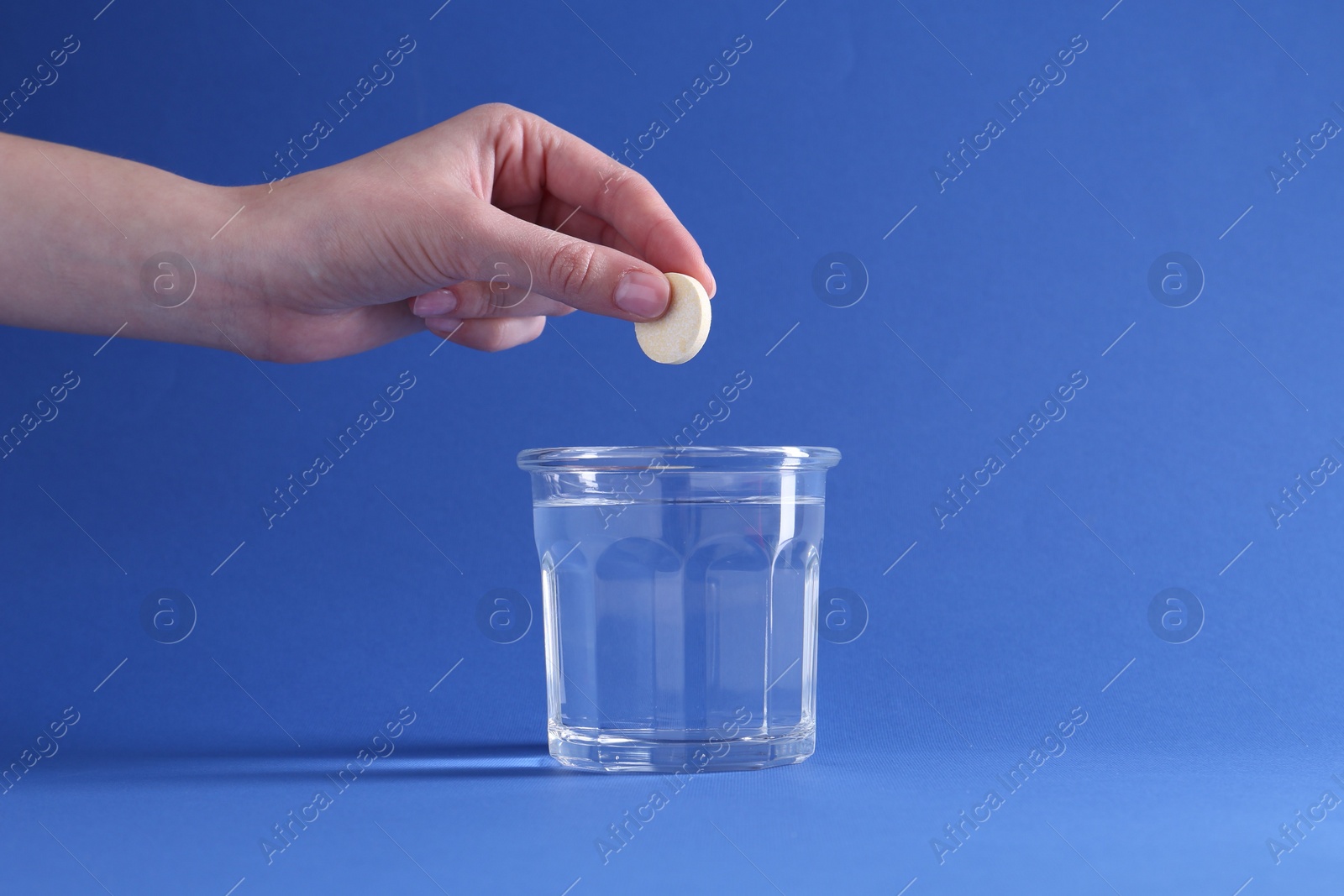 Photo of Woman putting effervescent pill into glass of water on blue background, closeup