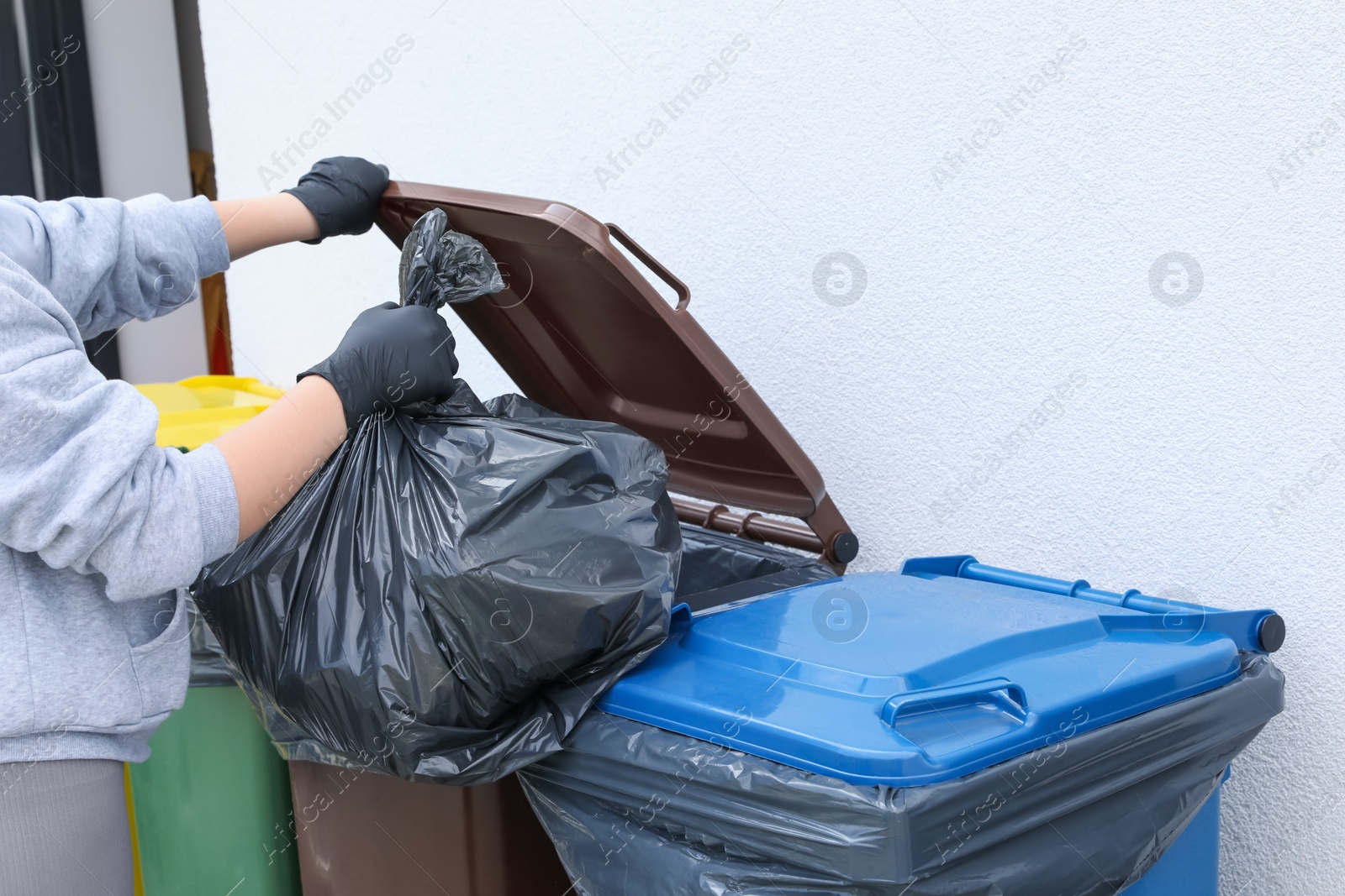 Photo of Woman throwing trash bag full of garbage in bin outdoors, closeup. Recycling concept