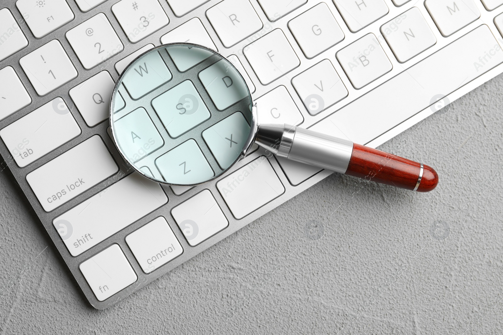 Photo of Magnifier glass and keyboard on light grey stone background, top view. Find keywords concept