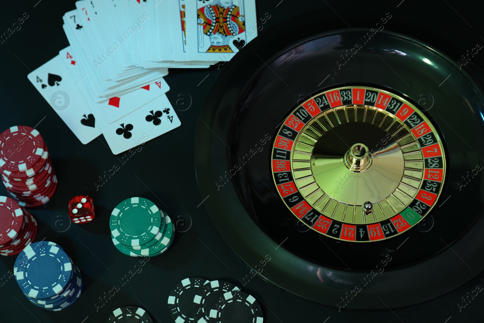 Photo of Roulette wheel, playing cards and chips on table, flat lay. Casino game