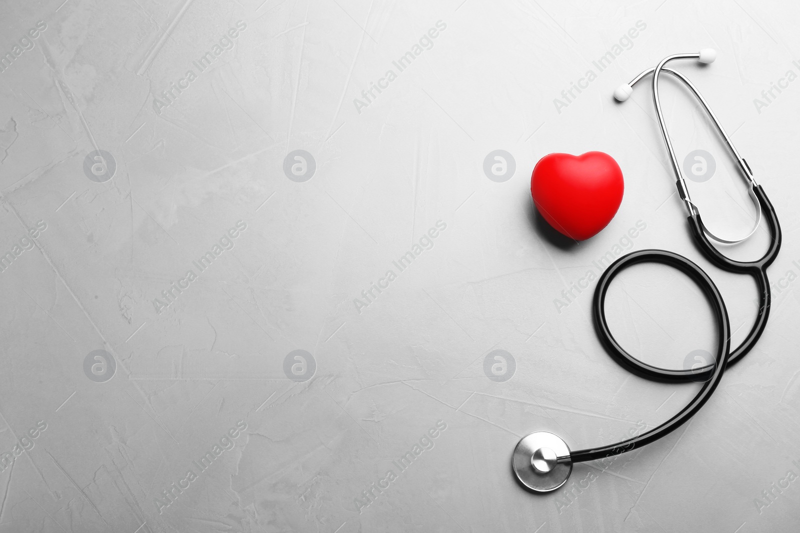 Photo of Stethoscope and red heart on grey background, flat lay with space for text