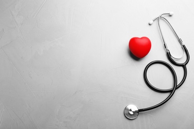 Stethoscope and red heart on grey background, flat lay with space for text