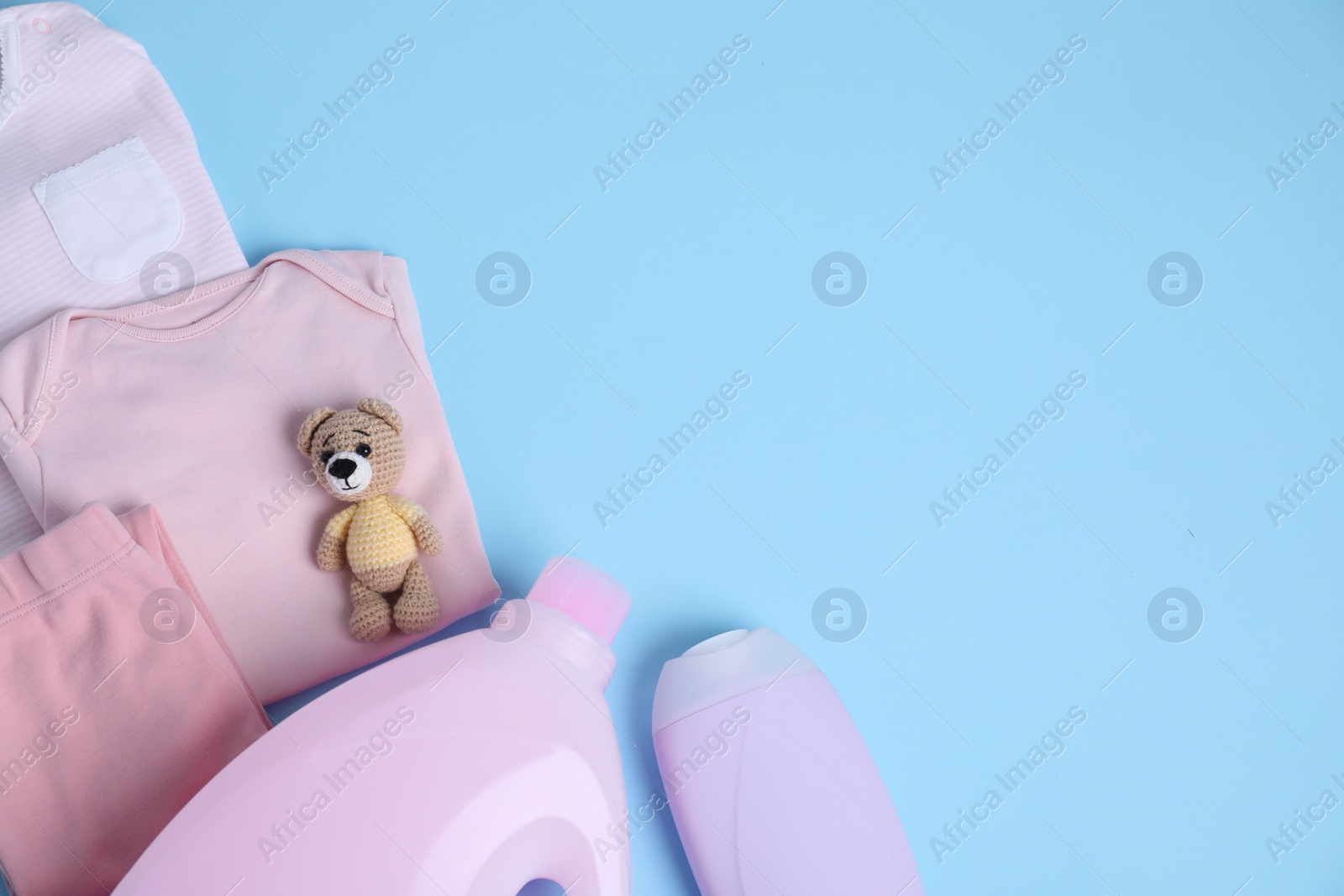 Photo of Bottles of laundry detergents, baby clothes and toy bear on light blue background, flat lay. Space for text