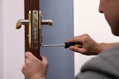 Photo of Handyman with screwdriver repairing door lock, closeup