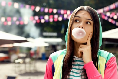 Beautiful young woman blowing chewing gum on city street outdoors