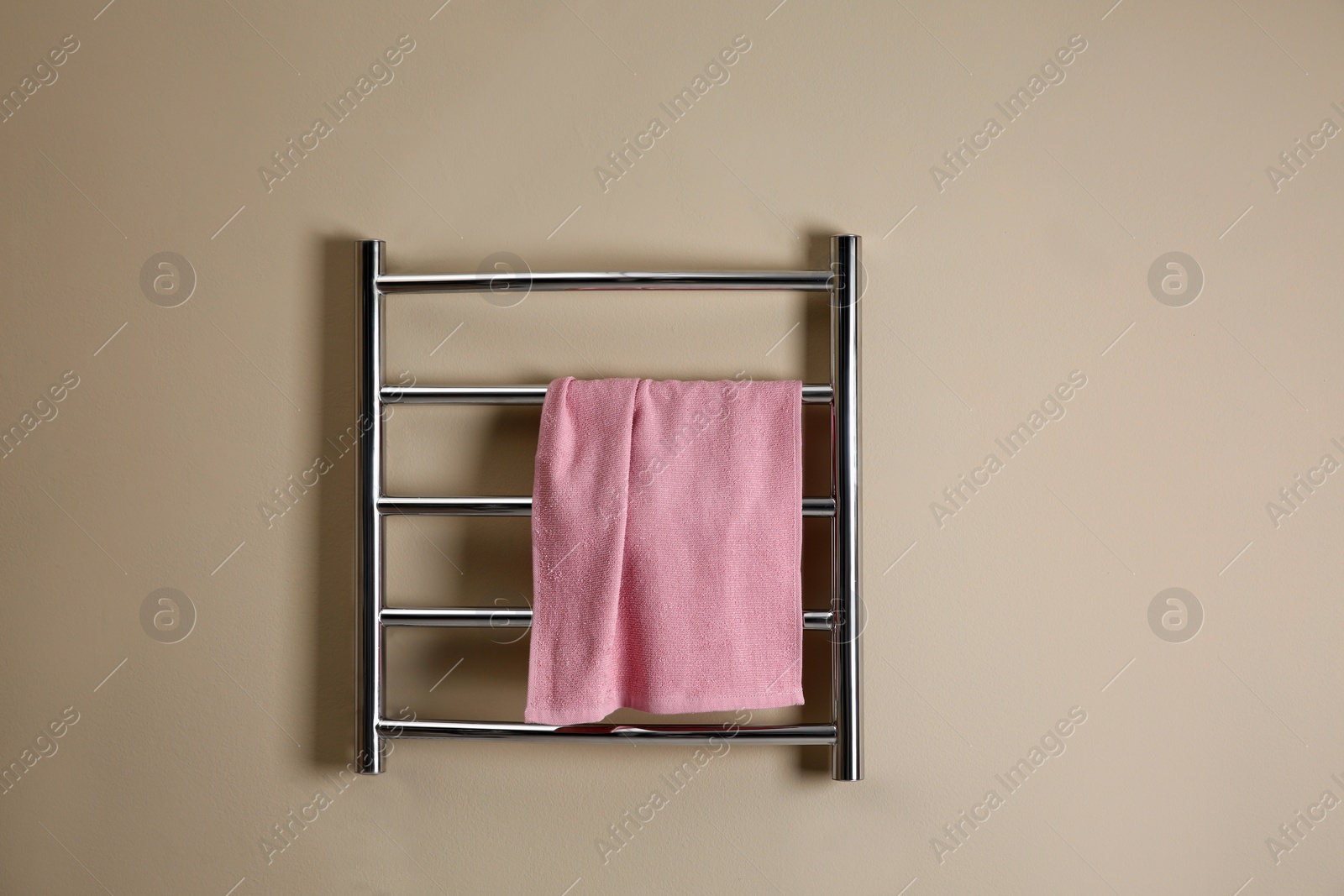 Photo of Modern heated towel rail with warm soft towel on beige wall