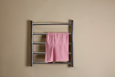 Modern heated towel rail with warm soft towel on beige wall