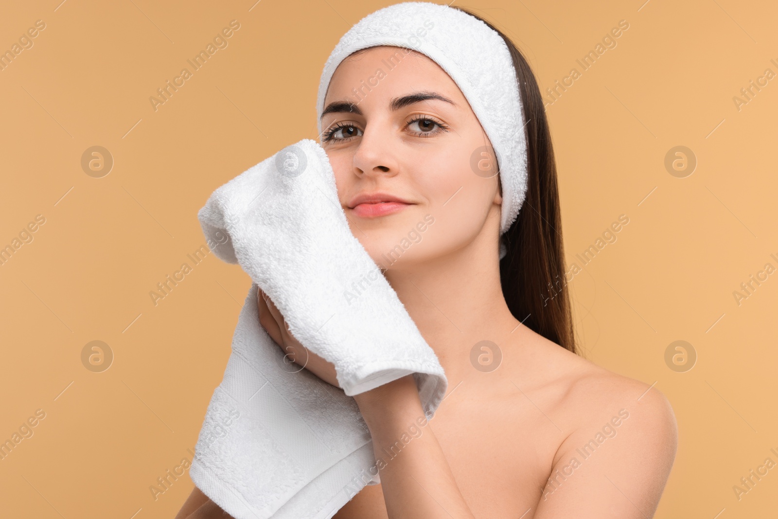 Photo of Washing face. Young woman with headband and towel on beige background