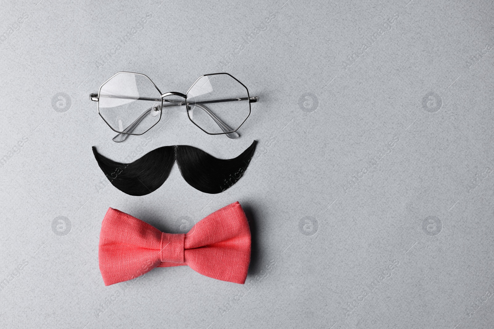 Photo of Man's face made of artificial mustache, bow tie and glasses on light grey background, top view. Space for text