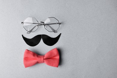 Man's face made of artificial mustache, bow tie and glasses on light grey background, top view. Space for text