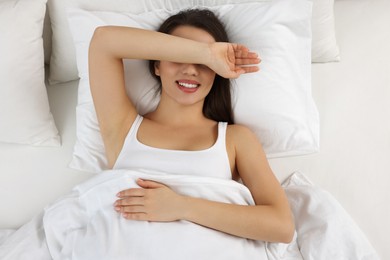 Happy young woman lying in bed, top view