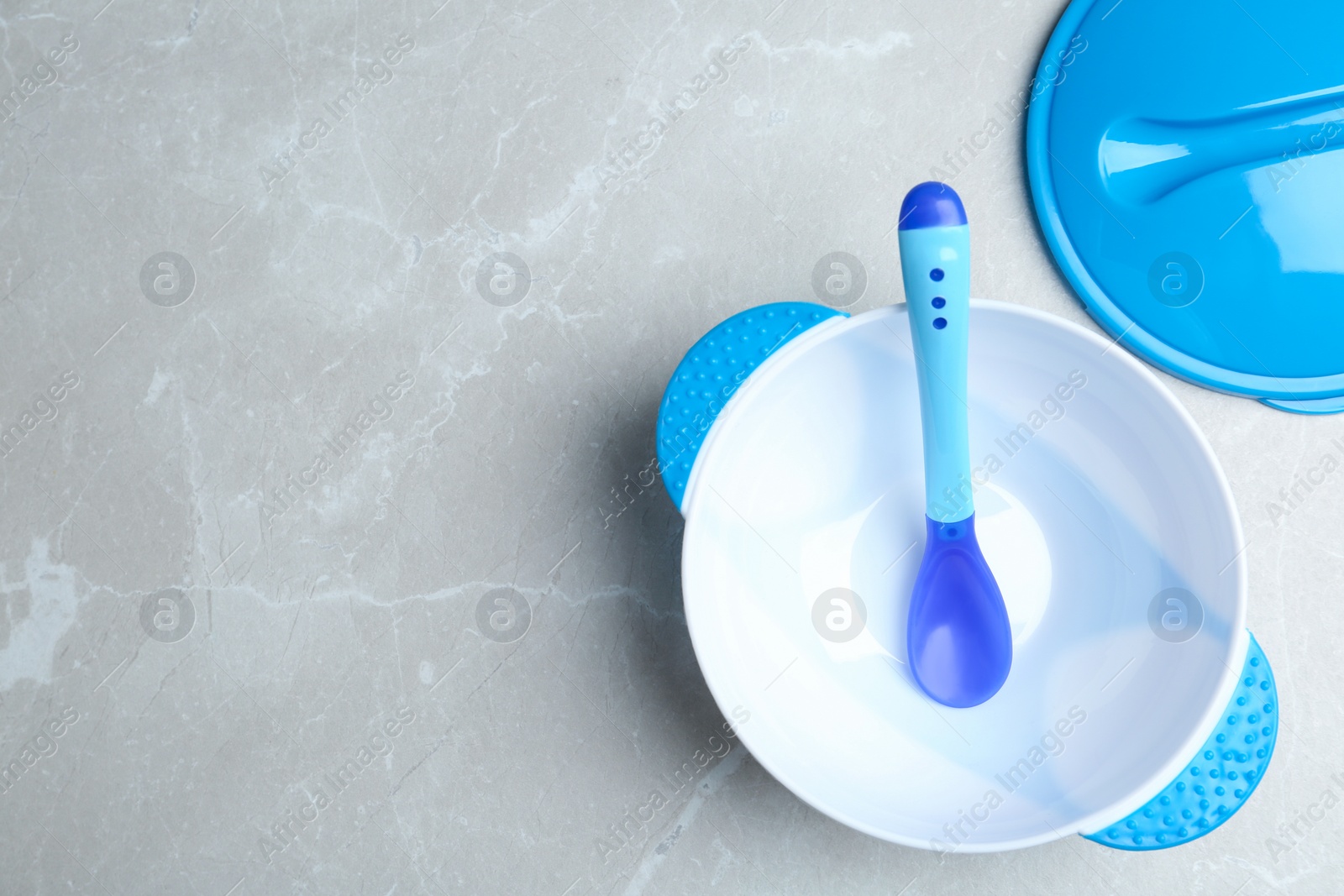 Photo of Plastic bowl and spoon on light grey marble table, flat lay with space for text. Serving baby food