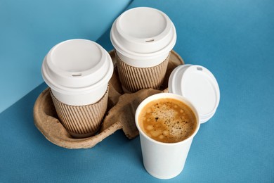 Photo of Takeaway paper coffee cups with sleeves, plastic lids and cardboard holder on blue background