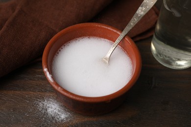 Photo of Chemical reaction of vinegar and baking soda in bowl on wooden table, closeup