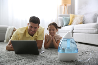 Father and daughter with laptop near modern air humidifier at home