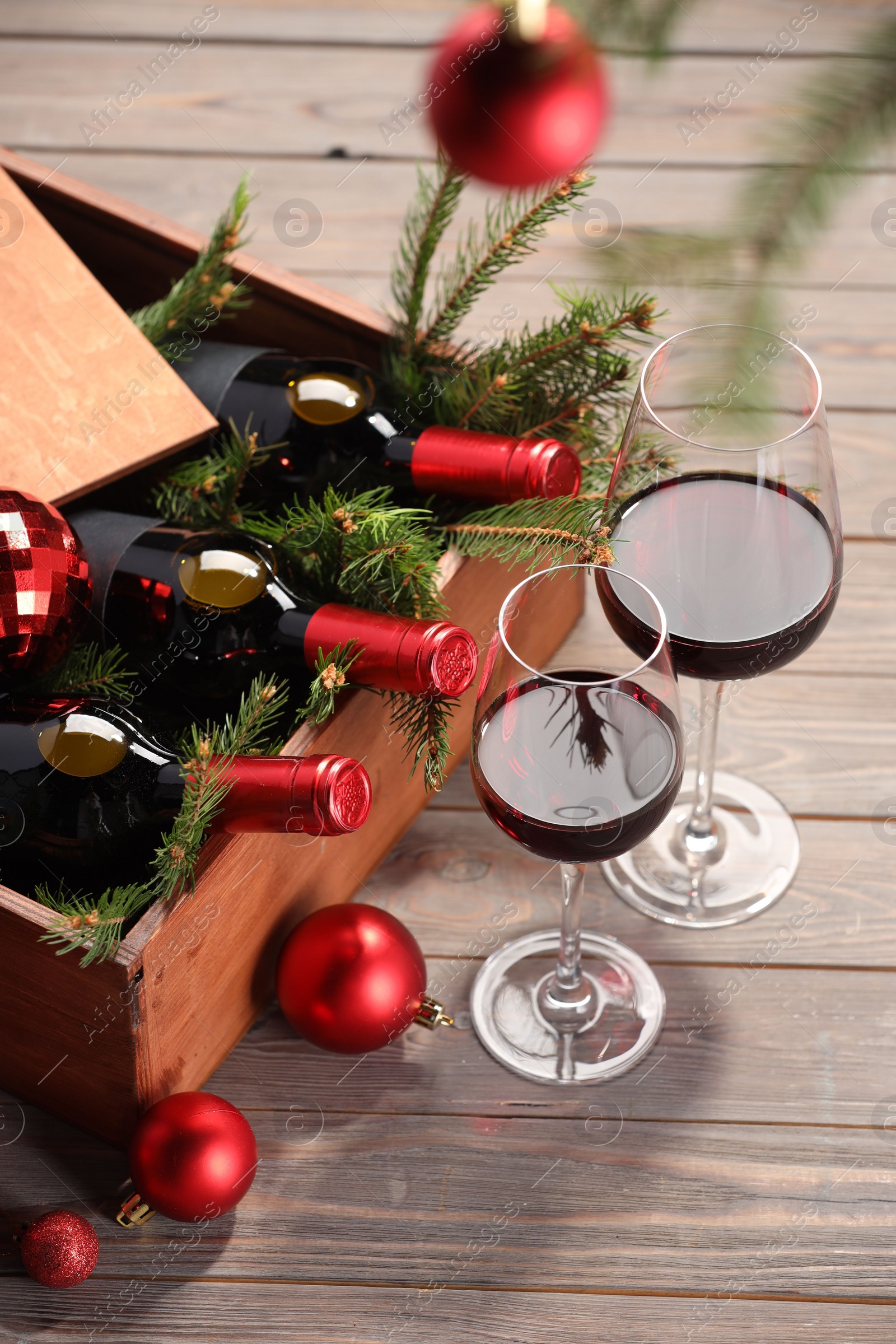 Photo of Wooden crate with bottles of wine, glasses, fir twigs and red Christmas balls on table