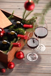 Wooden crate with bottles of wine, glasses, fir twigs and red Christmas balls on table