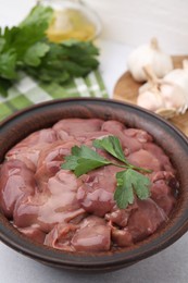 Photo of Bowl with raw chicken liver and parsley on white table, closeup