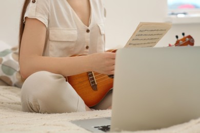 Photo of Woman learning to play ukulele with online music course at home, closeup. Time for hobby
