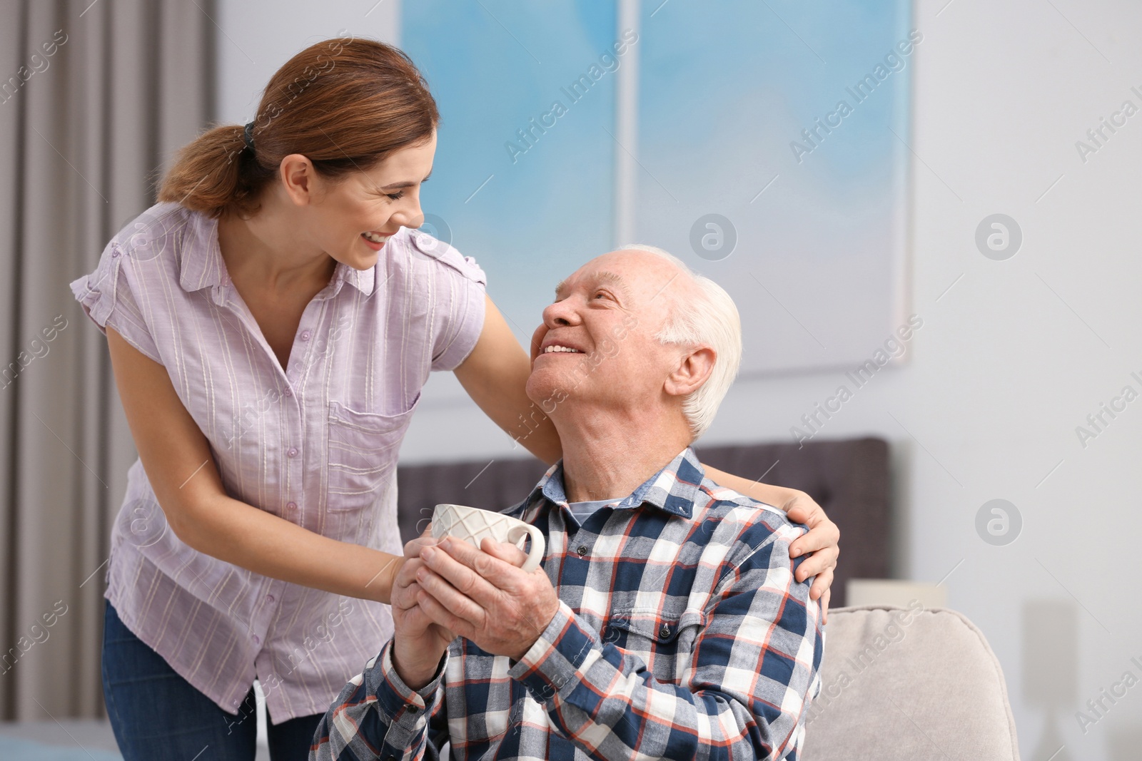 Photo of Elderly man with cup of tea near female caregiver at home. Space for text