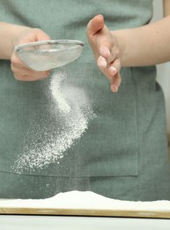 Photo of Woman sieving flour at table in kitchen, closeup