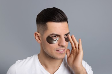Photo of Man applying dark under eye patch on grey background