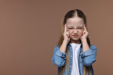 Little girl suffering from headache on brown background. Space for text