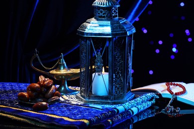 Arabic lantern, Quran, misbaha, Aladdin magic lamp, dates and folded prayer mat on mirror surface against blurred lights at night