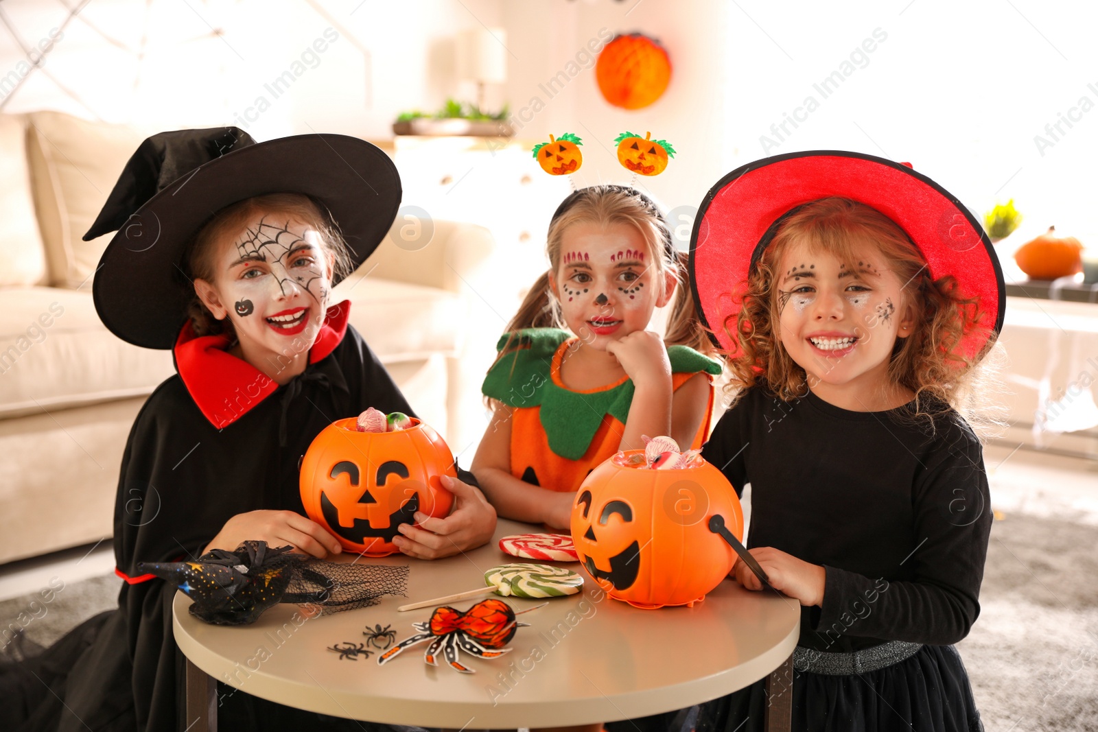 Photo of Cute little kids with pumpkin candy buckets wearing Halloween costumes at home