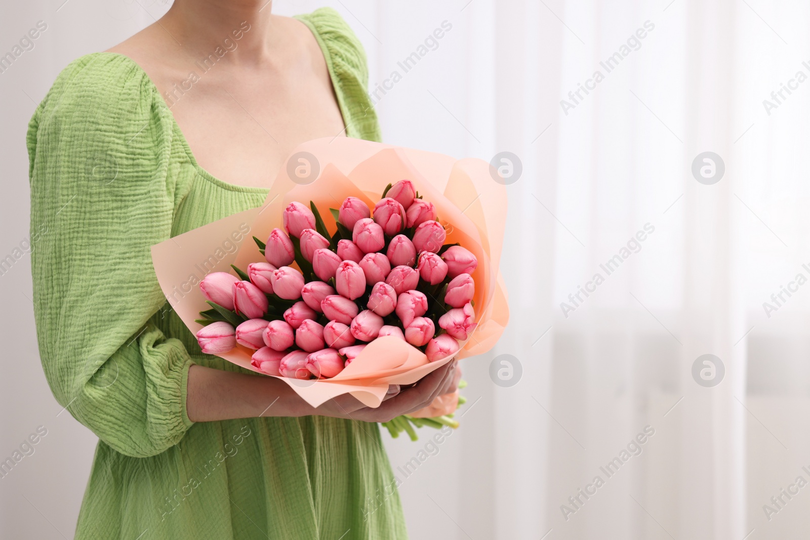 Photo of Woman holding bouquet of pink tulips indoors, closeup. Space for text