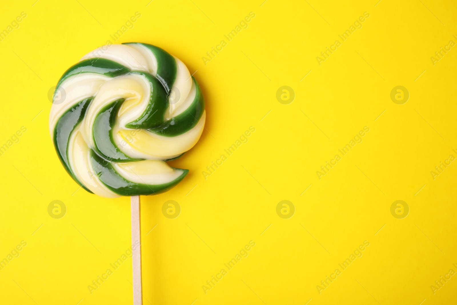 Photo of Colorful lollipop on yellow background, top view. Space for text