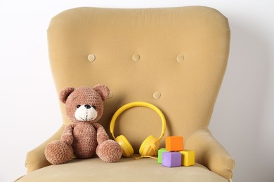 Photo of Baby songs. Toy bear, headphones and cubes on armchair near white wall