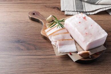 Photo of Pork fatback with rosemary, garlic and peppercorns on wooden table. Space for text