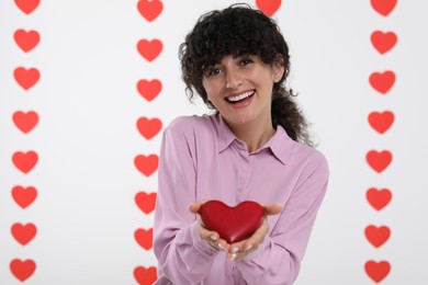 Photo of Happy young woman holding decorative red heart on decorated background