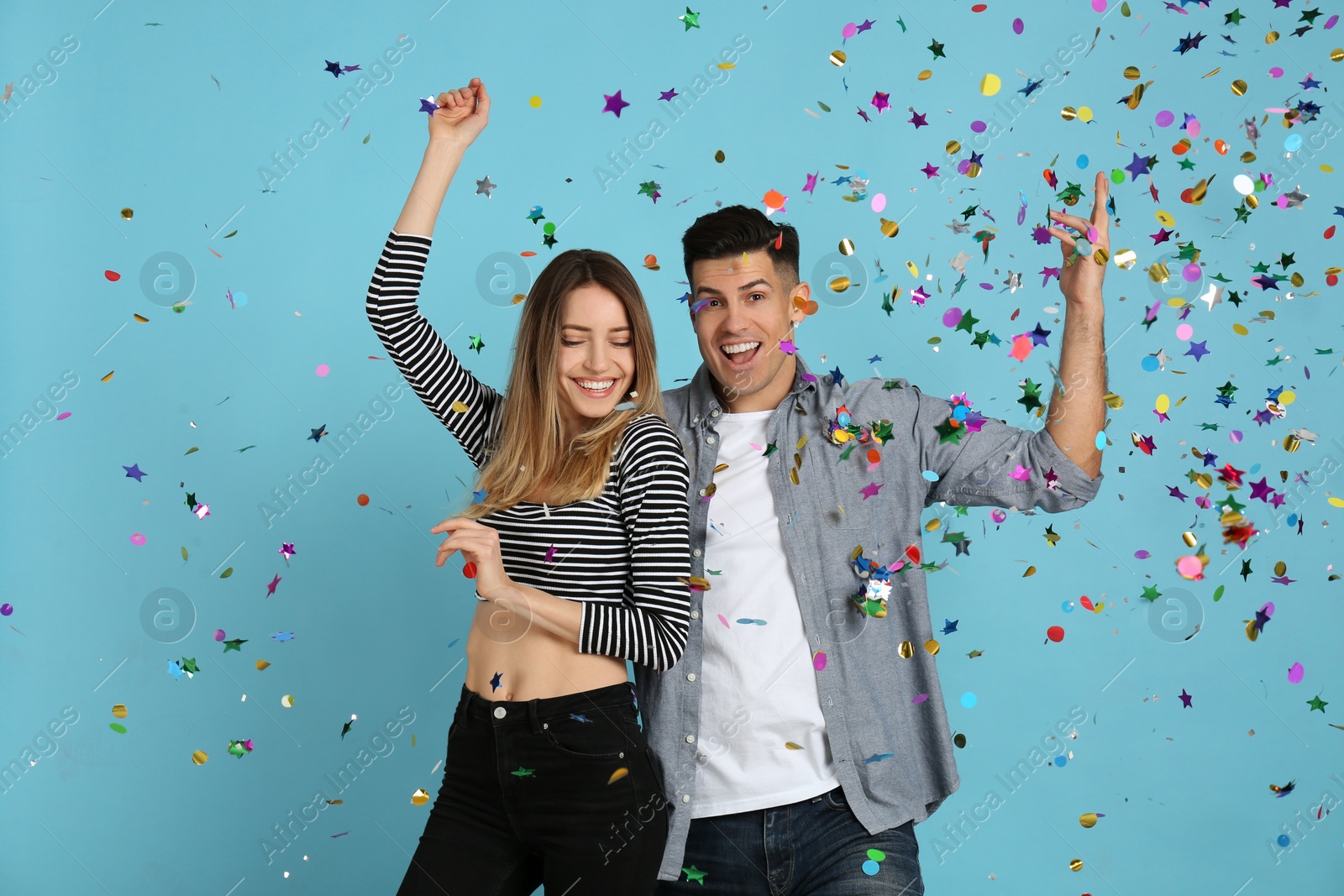 Photo of Happy couple and falling confetti on light blue background