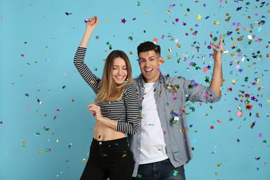 Happy couple and falling confetti on light blue background