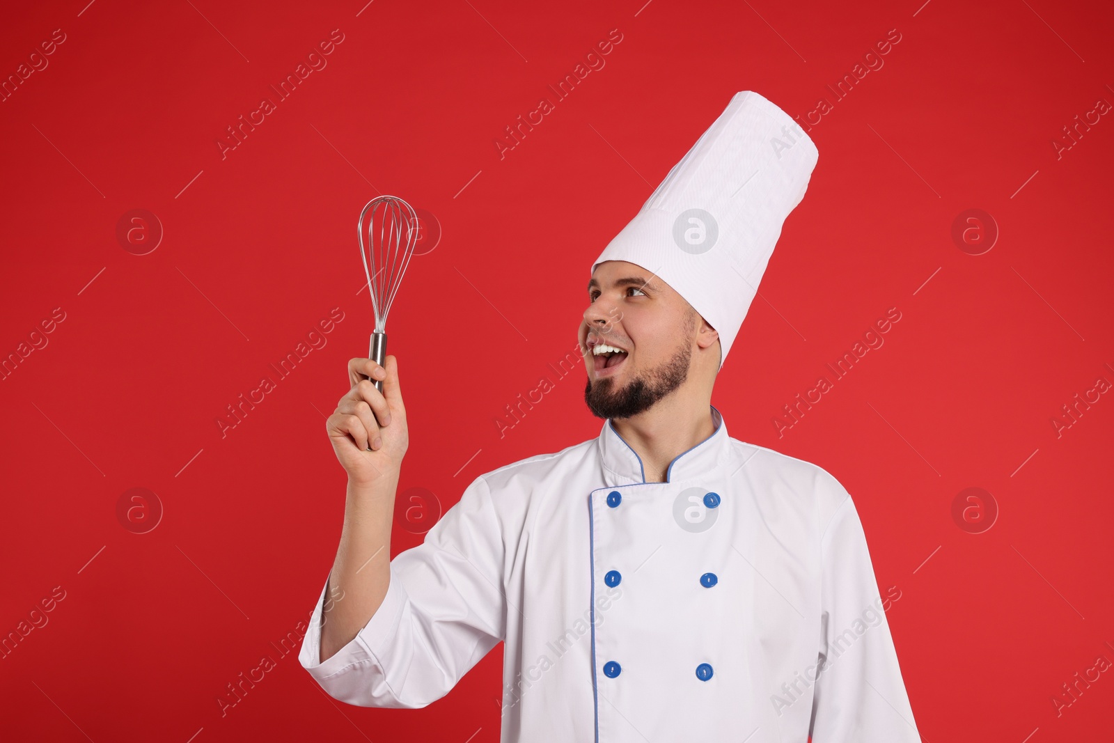 Photo of Happy professional confectioner in uniform holding whisk on red background