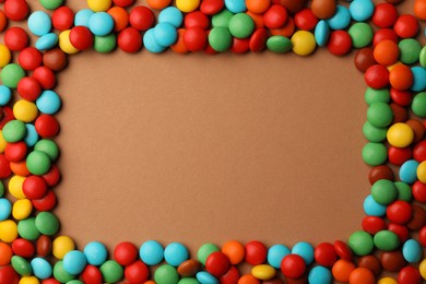 Photo of Frame of tasty colorful candies on light brown background, flat lay. Space for text