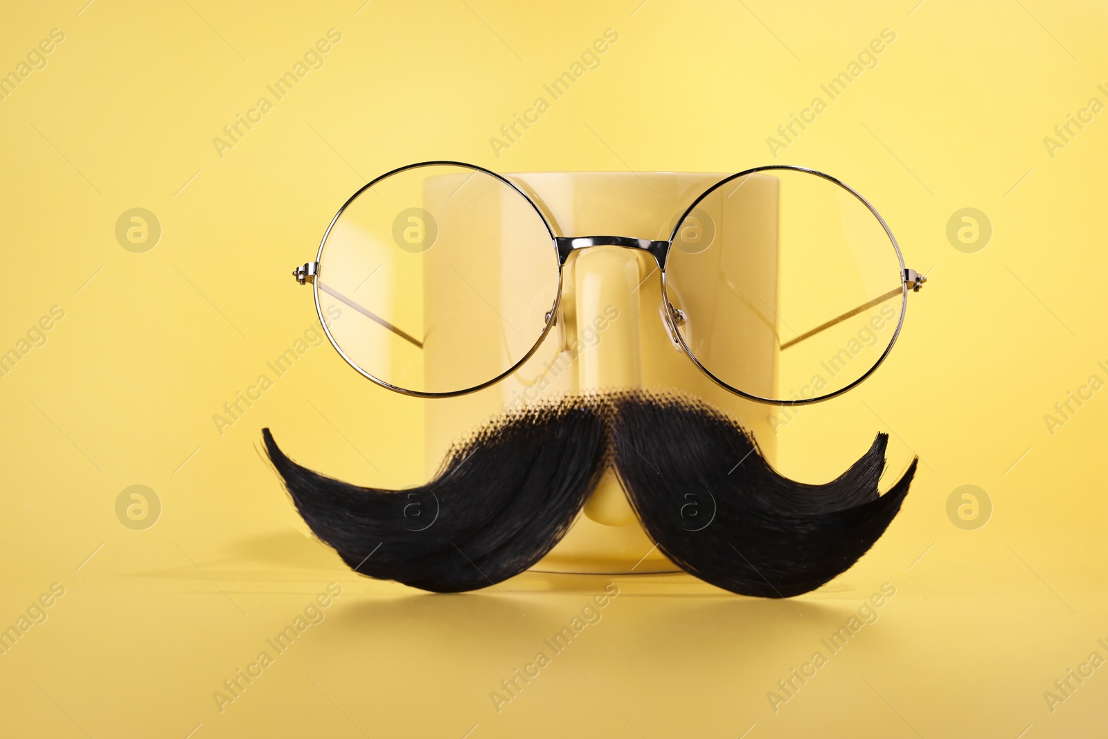 Photo of Man's face made of artificial mustache, glasses and cup on yellow background