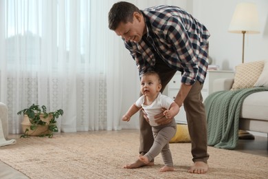 Photo of Father supporting his baby daughter while she learning to walk at home