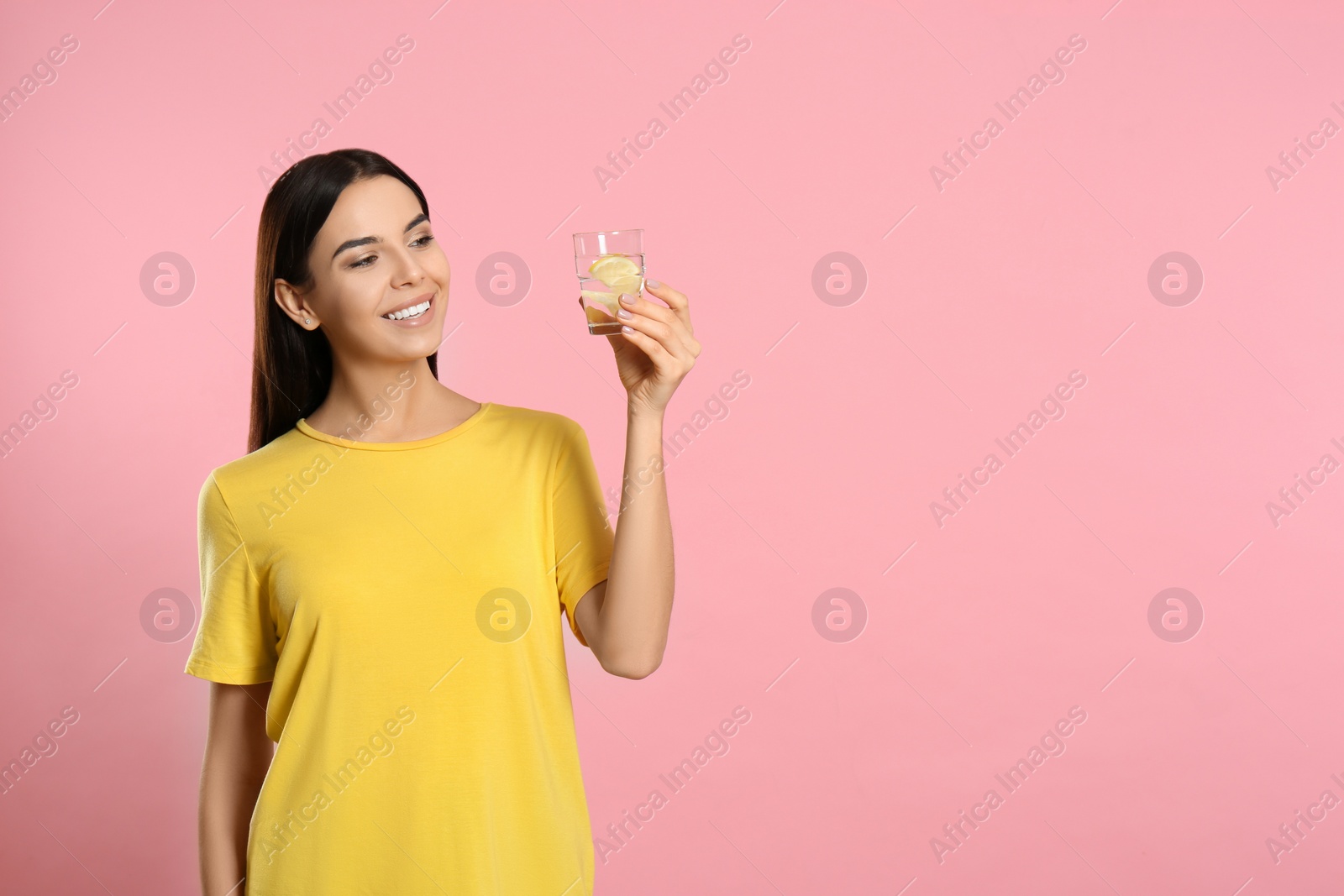 Photo of Beautiful young woman with tasty lemon water on pink background. Space for text