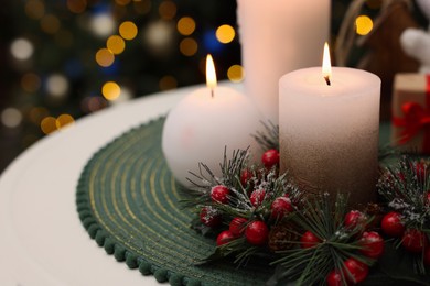 Photo of Beautiful burning candles and Christmas decor on white table against festive lights. Space for text