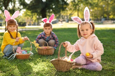 Photo of Cute little children hunting eggs in park. Easter tradition