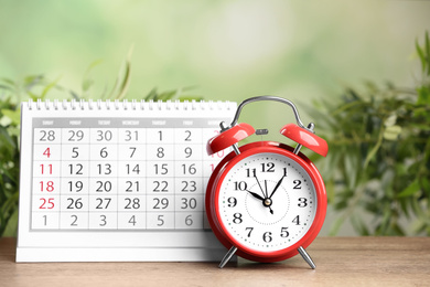 Photo of Calendar and alarm clock on wooden table against blurred green background